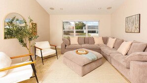 A living room with a sectional sofa, a white armchair, a small side table, a large mirror, and a potted plant. - Spacious Family Home | Saltwater Pool | Game Room (Palm Beach County)