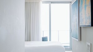 A bedroom with a bed, a large window with curtains, and a painting on the wall. - Oceanfront 36th Floor Condo with Stunning Views Resort and Beach Access (Hollywood)