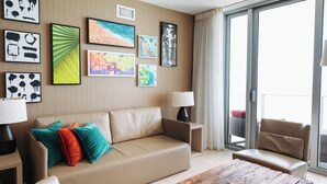 A modern living room with a beige sofa, colorful cushions, a wooden coffee table, and a large window with a view of the outdoors. - Oceanfront 36th Floor Condo with Stunning Views Resort and Beach Access (Hollywood)