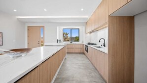 A modern kitchen with wooden cabinets, a white countertop, and a large window providing a view of the outdoors. - 4 Bedrooms, 3 Bathrooms, luxury homes for a vacation getaway. (Joshua Tree)