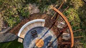 An outdoor seating area with a circular wooden table and four chairs, surrounded by a curved wooden bench.