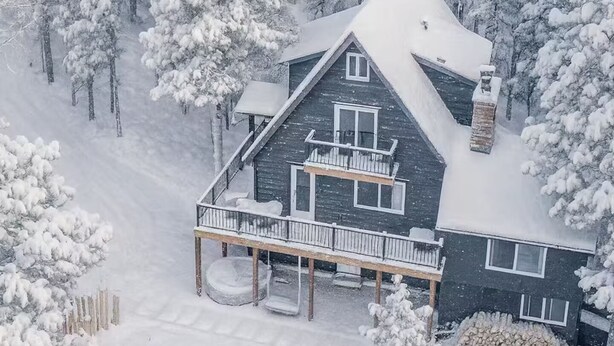 A snow-covered house with a balcony, a wooden deck, and a snow-covered yard.