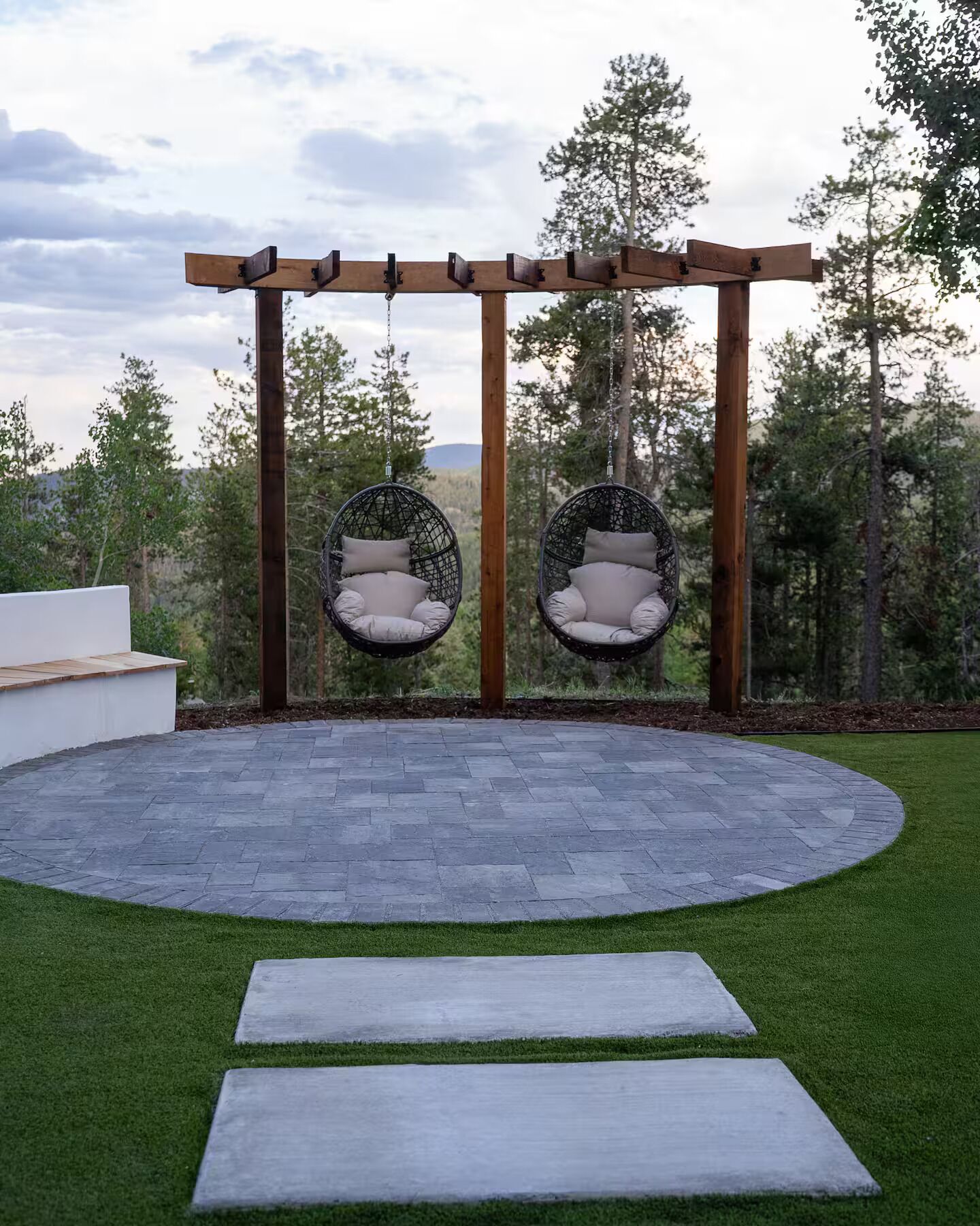 Un espacio de estar al aire libre con forma circular, con dos sillones colgantes y una pérgola.