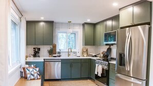 A modern kitchen with green cabinets, stainless steel appliances, and a large window providing natural light.