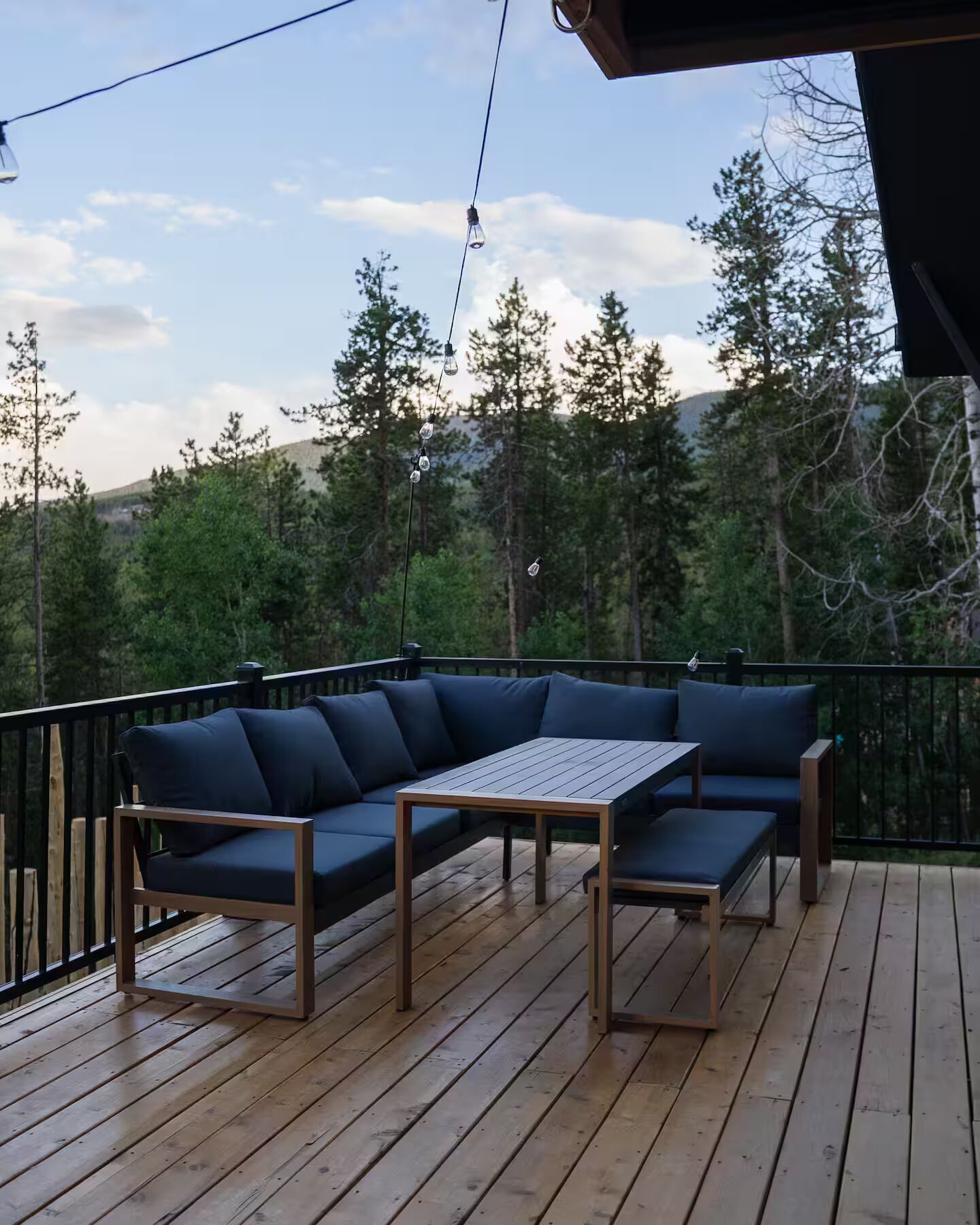 A wooden deck with a dark blue sectional sofa and a small table, surrounded by a black railing.