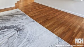 Una sala de estar moderna con un televisor de pantalla plana montado en una pared blanca, suelo de madera y un tapete grande abstracto.
