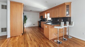 Una cocina moderna con gabinetes de madera, encimera de granito y tres taburetes de bar.