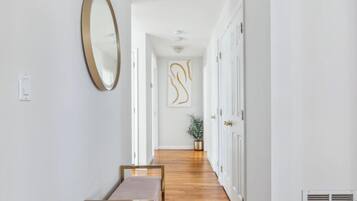 A hallway with a wooden floor, white walls, a round mirror, and a bench.