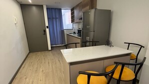 Una cocina compacta con una isla central, dos taburetes de bar y un refrigerador.