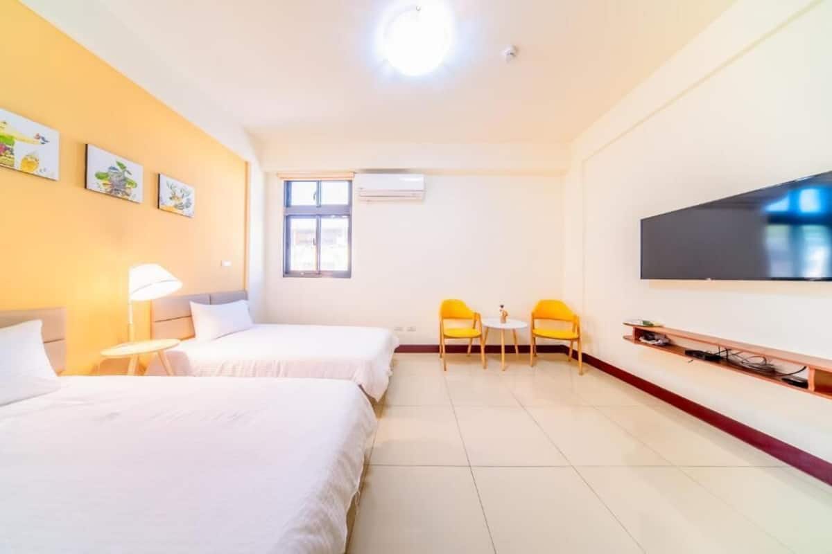 A hotel room with two beds, a TV, a window, and a small table with chairs.