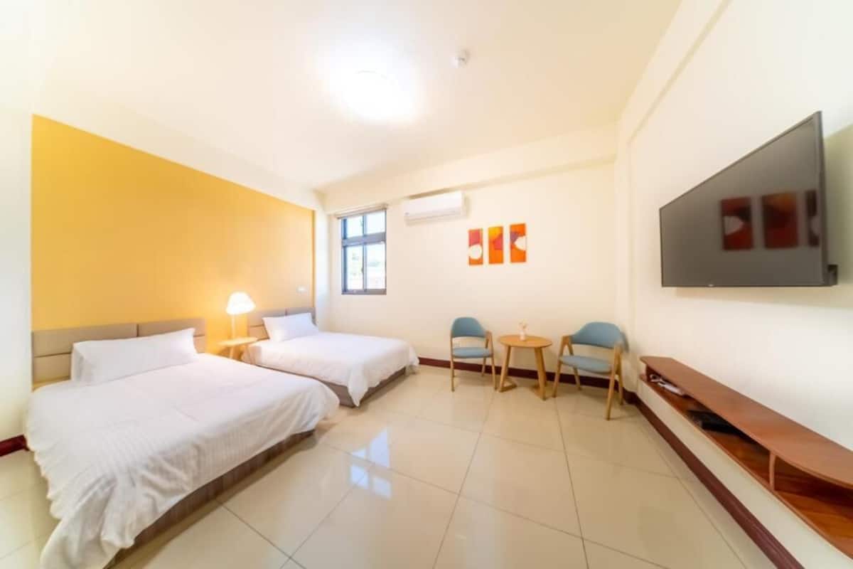 A hotel room with two beds, a TV, a small table, and chairs.