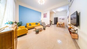 Un salon avec un canapé jaune, une table basse et un téléviseur fixé au mur.