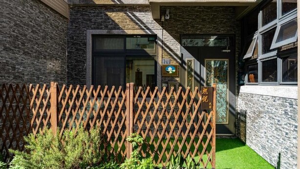 Un bâtiment doté d’une façade en pierre, d’une clôture en treillis de bois et d’une petite pelouse verdoyante.