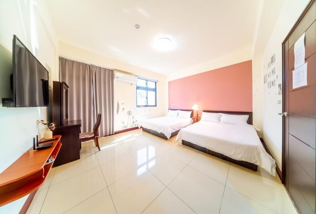 Habitación de hotel con dos camas, televisión, escritorio y ventana con cortinas.
