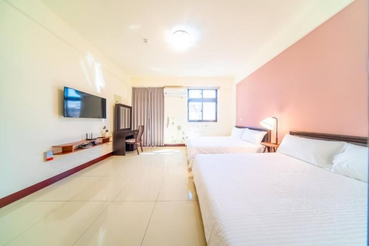 A hotel room with two beds, a TV, a desk, and a window.