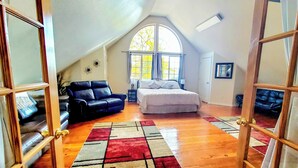 A bedroom with a bed, a black leather sofa, a window, and a wooden floor. - Explore Caves & Coast! Family-Friendly Oregon Stay (Cave Junction)
