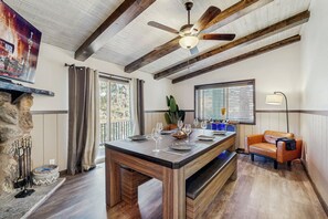 A dining area with a wooden table set for four, a stone fireplace, and a ceiling fan. - 2 Large Decks & Hot Tub! Big Bear Cabin Getaway (Big Bear)