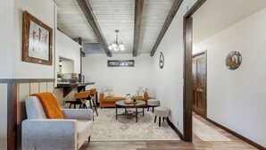 Amplia sala de estar con sofá, sillón y mesa de centro, piso de madera y techo con vigas a la vista.