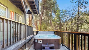 Un jacuzzi en una terraza con barandilla de madera, rodeado de árboles.