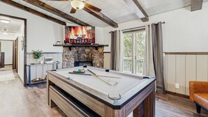 Una mesa de billar en una habitación con chimenea de piedra, vigas de madera y un ventilador de techo.