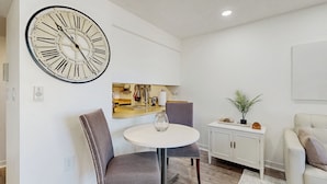 A modern living room with a round table, two chairs, a large wall clock, a white cabinet, and a small plant. - Mtn-View Balcony: Condo 6 Mi to Dtwn Phoenix (Phoenix)