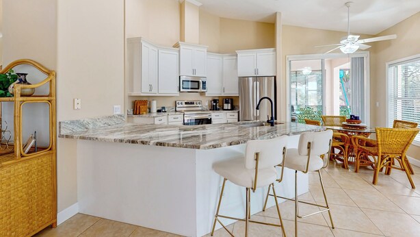 A modern kitchen with white cabinetry, a marble countertop, and a central island with bar stools. - Golfer's Oasis w/ Pool in Black Diamond Ranch! (Lecanto)