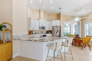 A modern kitchen with white cabinetry, a marble countertop, and a central island with bar stools. - Golfer's Oasis w/ Pool in Black Diamond Ranch! (Lecanto)