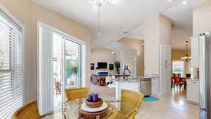 A spacious living area with a glass dining table surrounded by wicker chairs, a kitchen with white cabinets, and a large sliding glass door leading to an outdoor patio. - Golfer's Oasis w/ Pool in Black Diamond Ranch! (Lecanto)