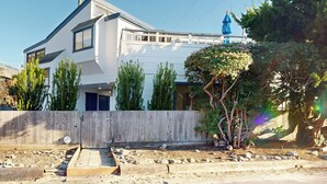 A modern two-story house with a white exterior, a wooden fence, and a landscaped garden with trees and shrubs. - Stroll to Shore: Stinson Beach Gem w/ Hot Tub (Stinson Beach)