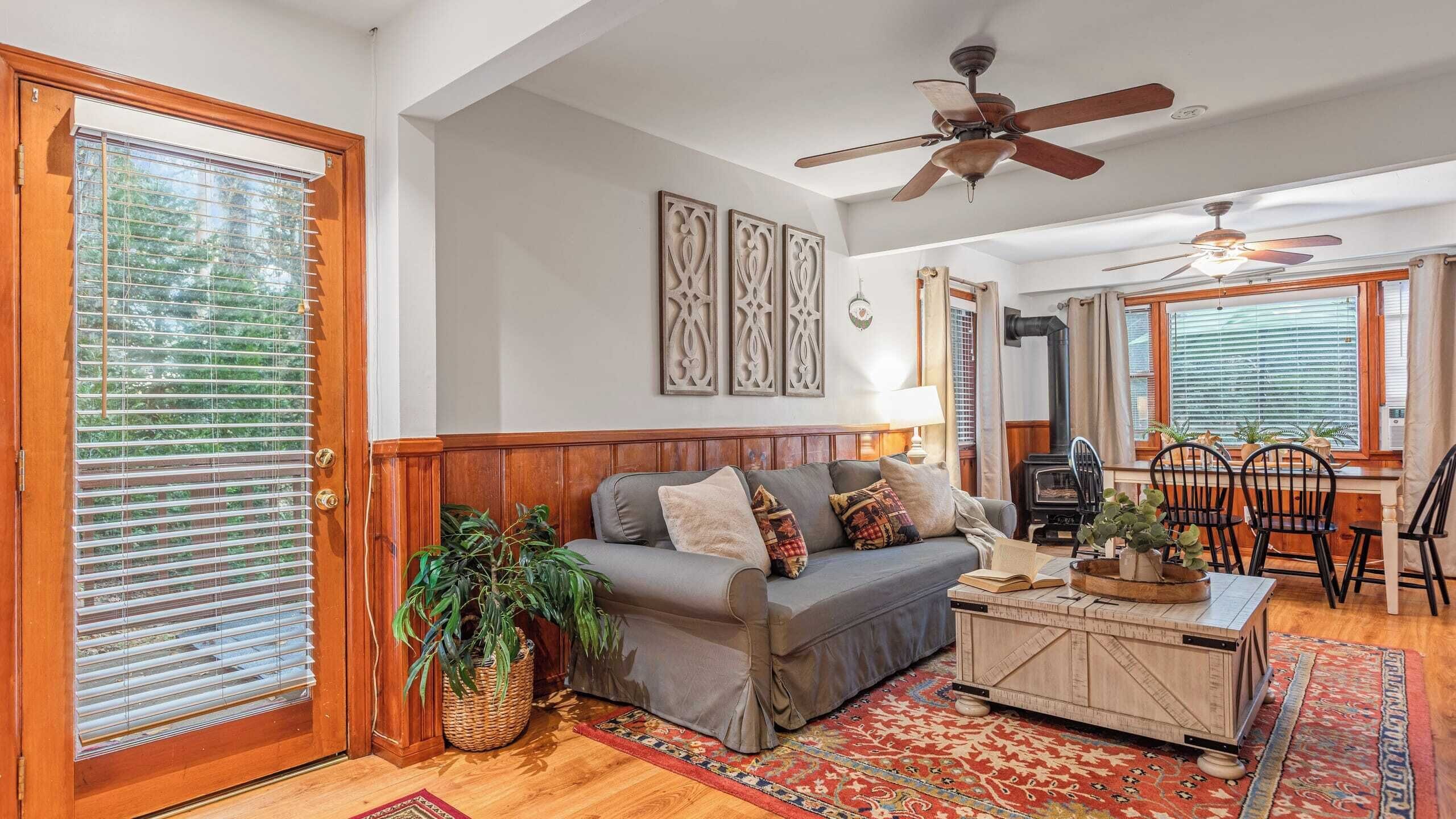 A cozy living room with a grey sofa, wooden floor, and a red patterned rug.
