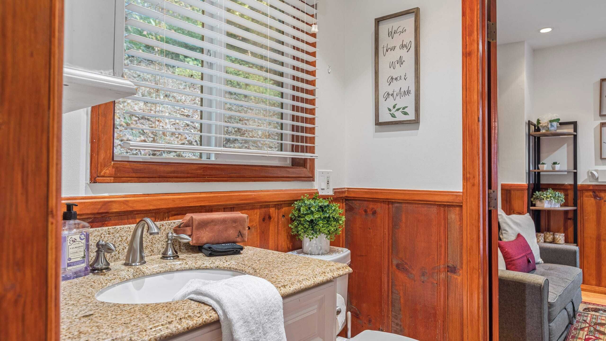A bathroom with a granite countertop, a sink, a mirror, and a window with blinds.