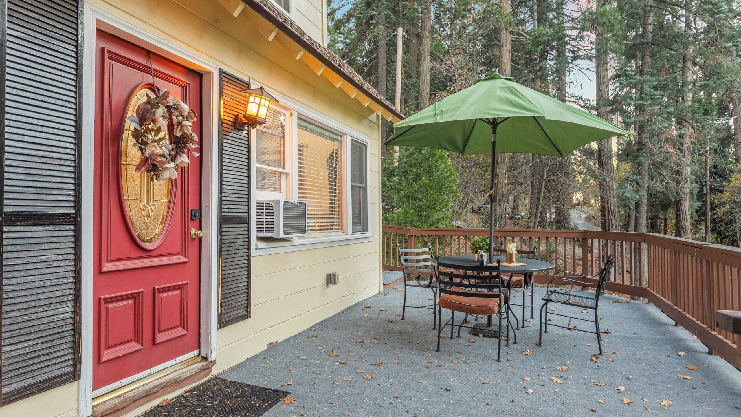 A house with a red door, a porch with a table and chairs, and a green umbrella.