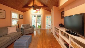 Una sala de estar con techo de madera, un televisor de pantalla plana grande, un sofá, una mesa de centro y un mueble de televisión con estantes.
