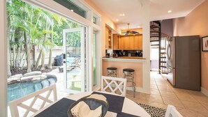 Una cocina moderna con barra, un comedor con vistas a una piscina y una escalera que sube a un altillo.