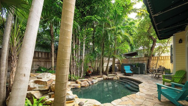 Un patio trasero con piscina, terraza de piedra y mobiliario exterior.