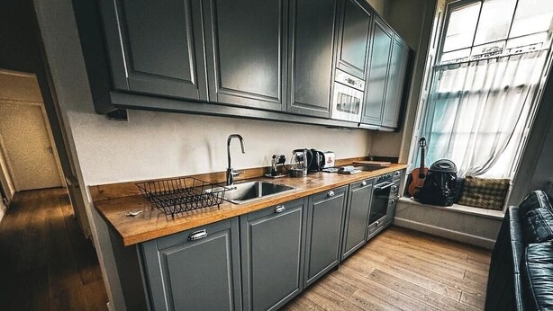 A modern kitchen with grey cabinets, a wooden countertop, and a window with curtains.