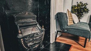 A black fireplace with intricate designs, a grey sofa with a patterned cushion, and a wooden floor.