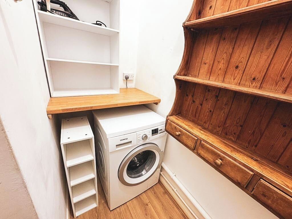 Een kleine wasruimte met een wasmachine, houten planken en een witte kast.