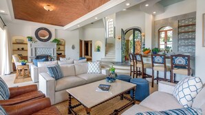A spacious living room with a high ceiling, a fireplace, and a dining area with chairs and a table. - Casa Primera: 6BR Ocean-View Villa, Palmilla Dunes Club Access (San Jose del Cabo)