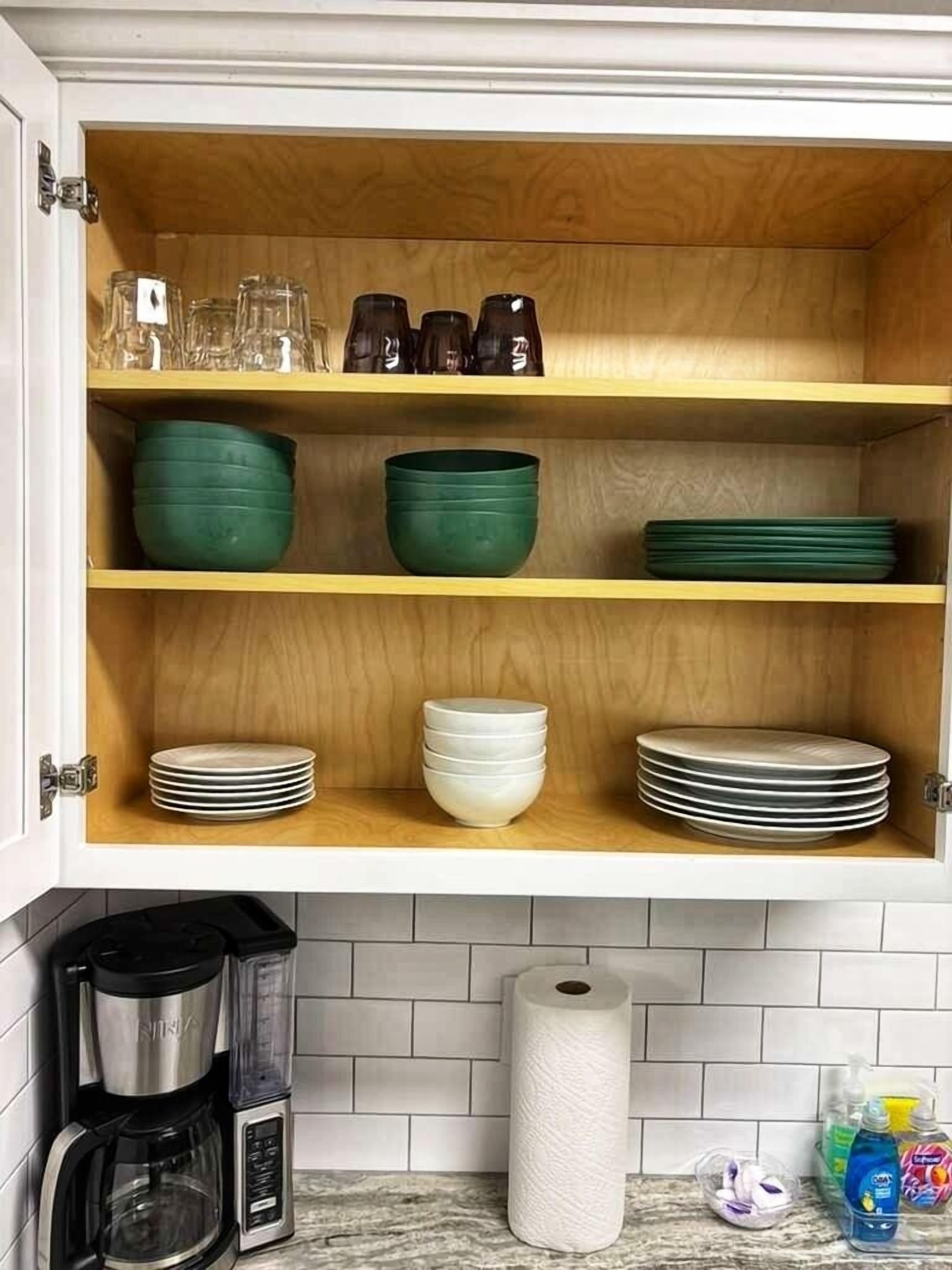 Un armario de cocina con cristalería, cuencos verdes y platos apilados.