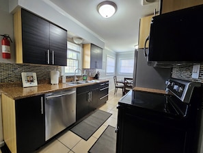 A modern kitchen with stainless steel appliances, a granite countertop, and a dining area with a table and chairs. - Spacious 5-bedroom house in charming Ypsilanti with AC (Ypsilanti)