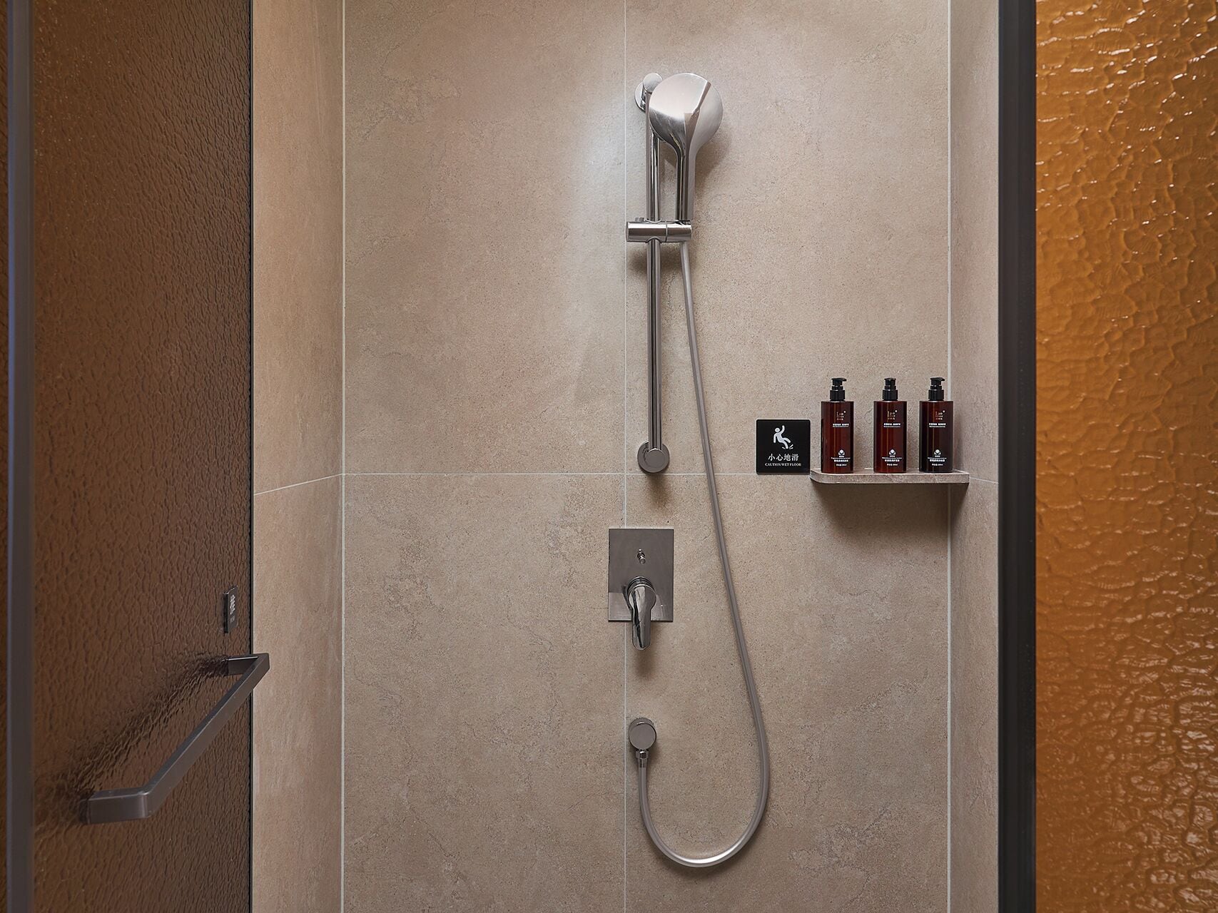 Une douche moderne dotée d’un pommeau de douche à main, d’un panneau de commande mural et d’une étagère pour les articles de toilette.