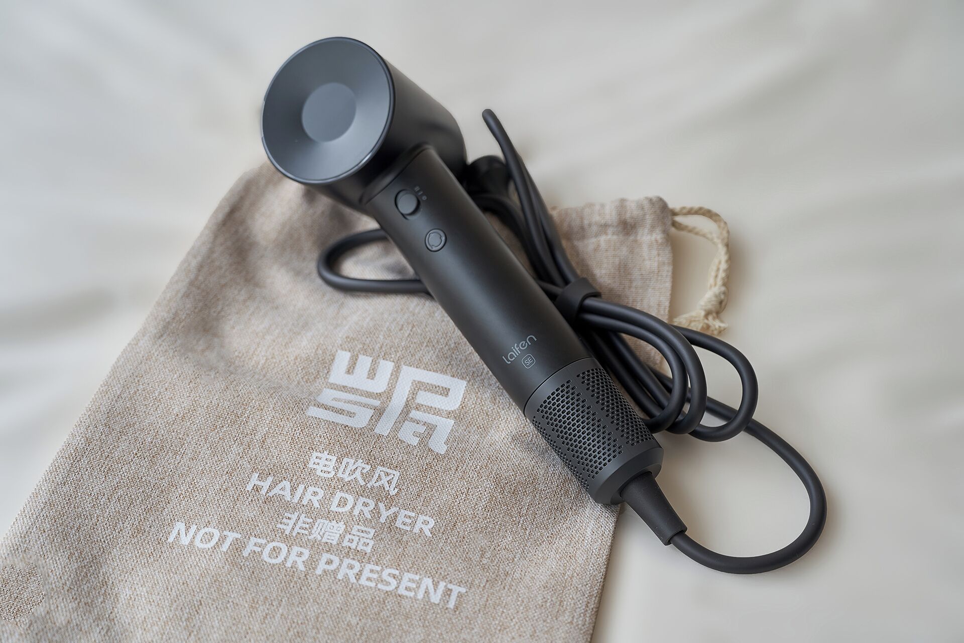 A hair dryer with a cord and a power button, placed on a beige cloth with text.