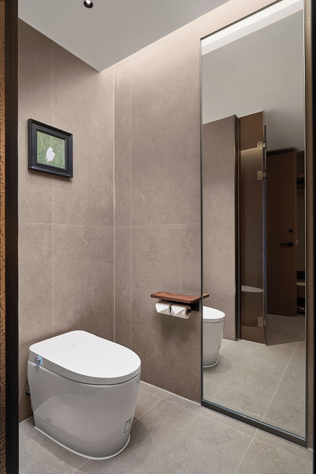 Un baño moderno con inodoro, un estante pequeño y un cuadro en la pared.