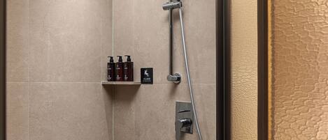 A shower with a handheld showerhead, a wall-mounted control panel, and a shelf with toiletries.