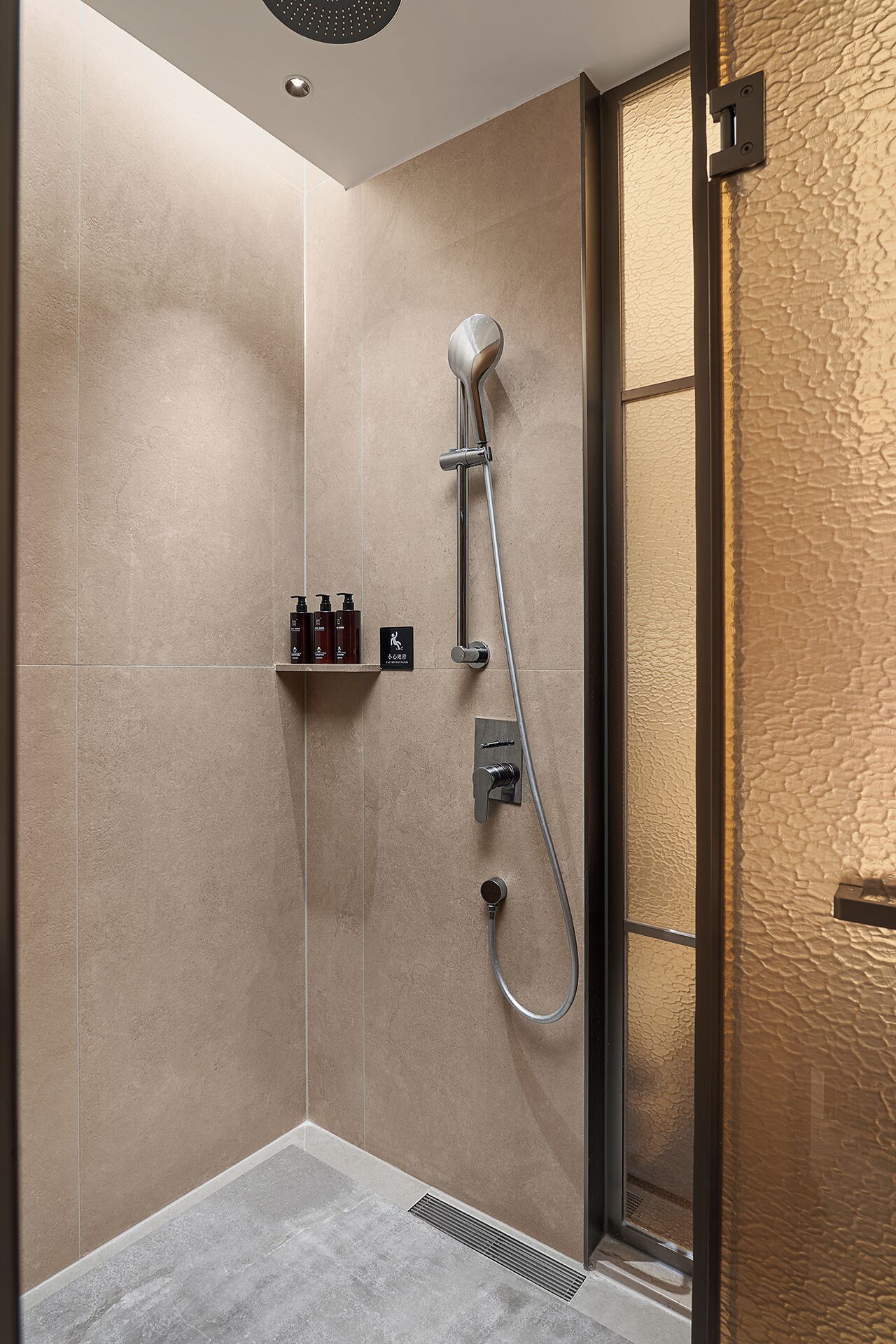 A modern shower area with a handheld showerhead, a wall-mounted control panel, and a shelf with toiletries.