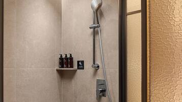 A modern shower area with a handheld showerhead, a wall-mounted control panel, and a shelf with toiletries.