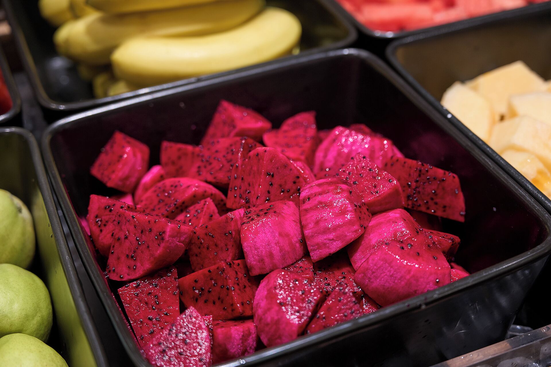 A selection of fruits including dragon fruit and bananas in a container.