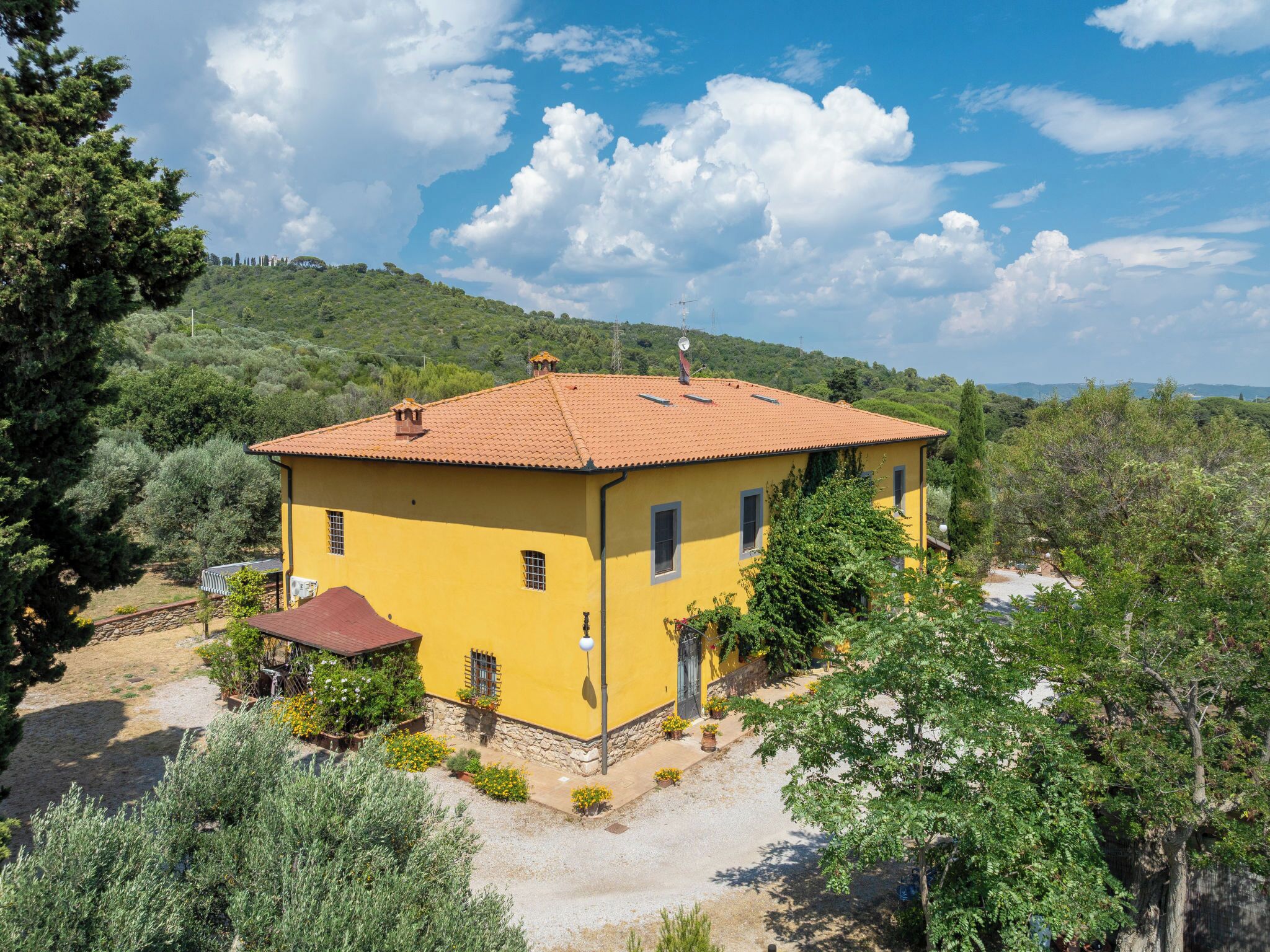 Un bâtiment jaune, surmonté d’un toit en tuiles, entouré de verdure et de collines.