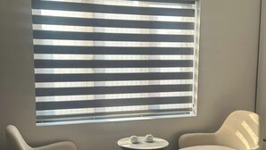 A modern room with a large window covered by horizontal blinds, two white armchairs, and a small round table with a teapot and cup. - Elegant Hotel (Hanoi)